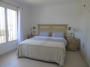 A bedroom with a bed, two bedside tables, a nightstand, a window with curtains, and a wall with a decorative plate. - Apartment 'Residencia La Fuente' with Shared Pool, Wi-Fi and Air Conditioning (Mijas)