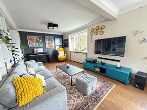 Ein modernes Wohnzimmer mit einem grauen Sofa, einem gelben Überwurf, einem gelben Sessel, einem Couchtisch, einem Fernseher, einer blauen Unterhaltungseinheit und einem Klavier.