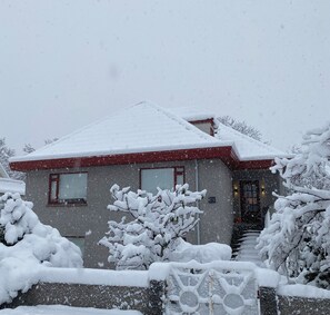 A house with a snow-covered roof and windows, surrounded by snow-laden trees and a fence. - Family Friendly House by Laugardalur Park & Pool, 2.5. km from Downtown (Reykjavík)