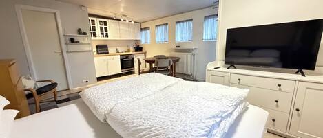 A hotel room with a bed, a TV, a kitchenette, and a dining area.