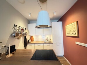 A modern kitchen with white cabinets, a black induction cooktop, and a hanging pot rack. - Cosy and family friendly apartment in Reykjavik, Great location ! (Reykjavík)