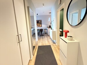 A hallway leading to a dining area with a painting on the wall, a lamp, and a red object on a white cabinet. - Cosy and family friendly apartment in Reykjavik, Great location ! (Reykjavík)