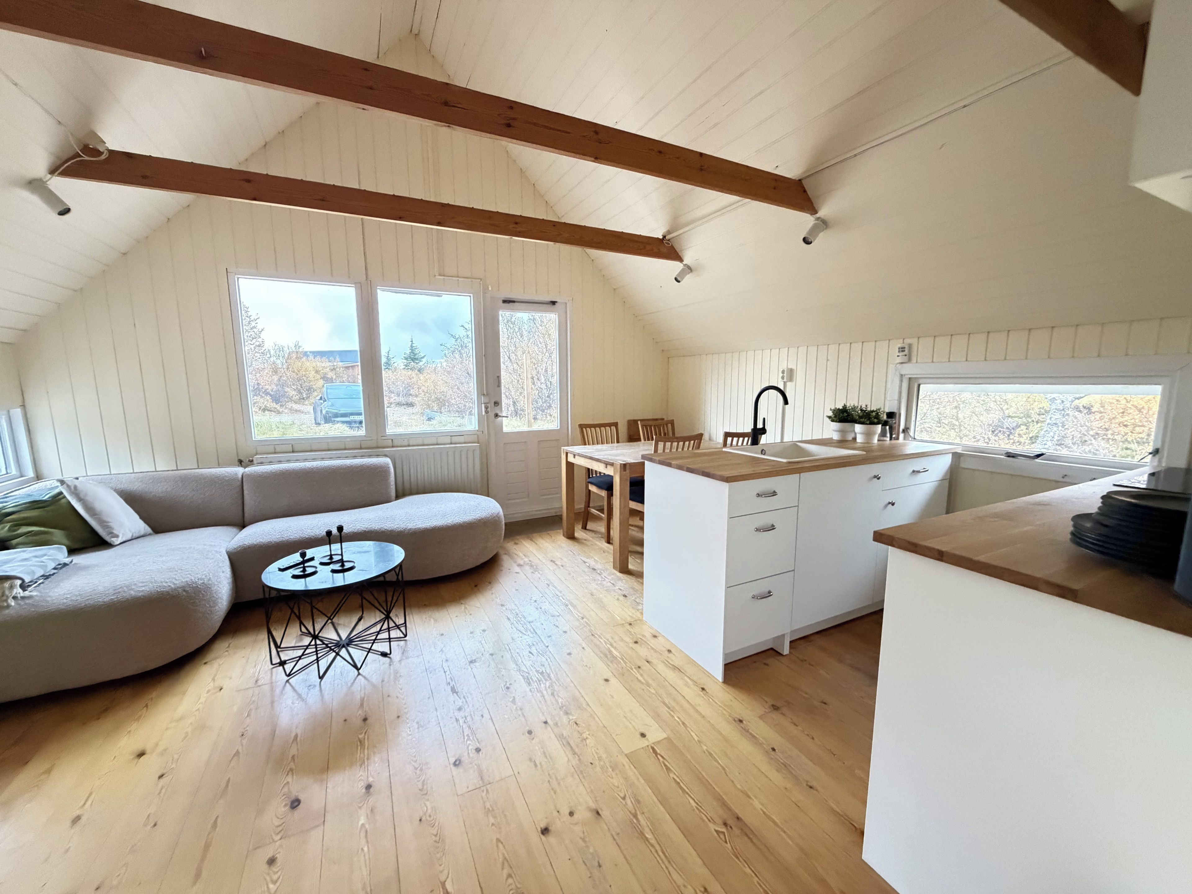 Um espaço de estar acolhedor em estilo loft, com um sofá curvo, uma mesa redonda pequena e uma cozinha com pia e bancada.