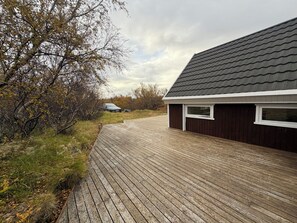 A wooden deck leading to a building with a dark roof and white trim. - Cosy cabin in Húsafell in Iceland, with Hot Tub. (Húsafell)