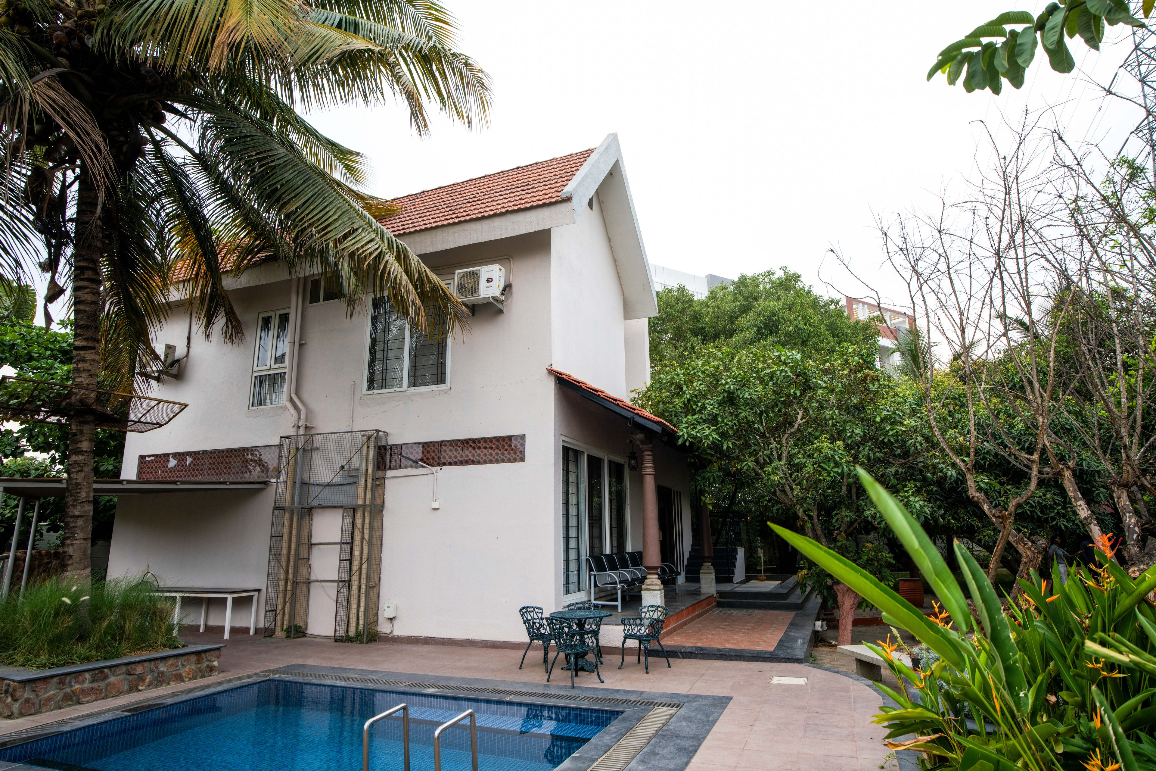 Un edificio de dos pisos con piscina, mobiliario exterior y una palmera.