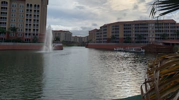A hotel with multiple floors, a water fountain, and a boat docked near the water.