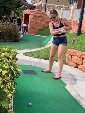 Una persona jugando minigolf en un campo de césped artificial verde con una pelota morada.