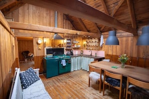 A cozy cabin interior with a wooden dining area, a kitchenette, and a sleeping area with a sofa and a bed.
