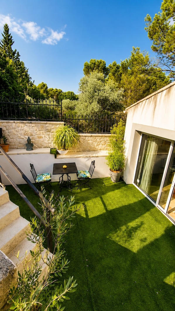 A modern outdoor patio with a dining table and chairs, a stone wall, and a grassy lawn. - New Listing (Pertuis)
