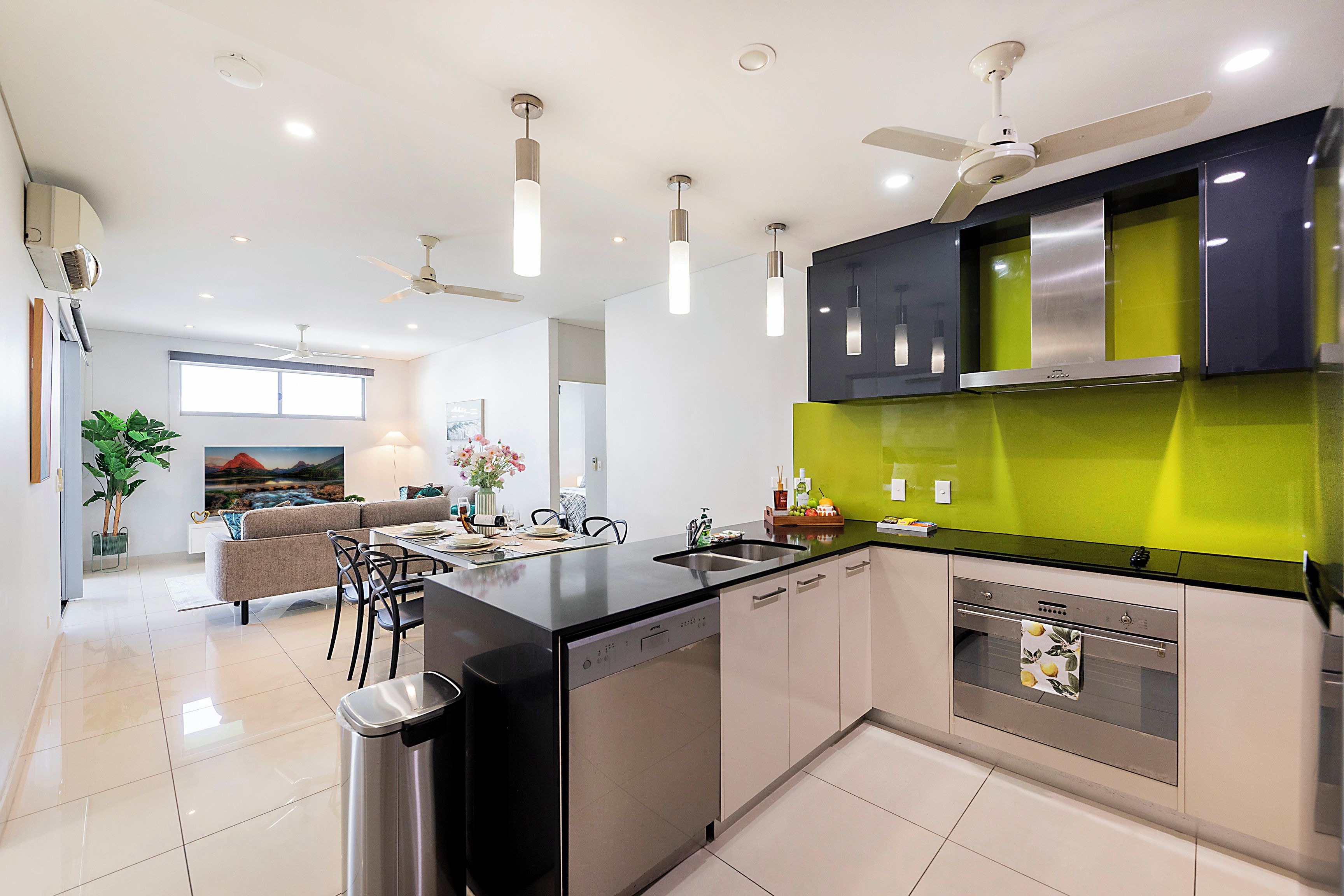 A modern kitchen with a central island, a dining area with a sofa and chairs, and a living room with a large window.