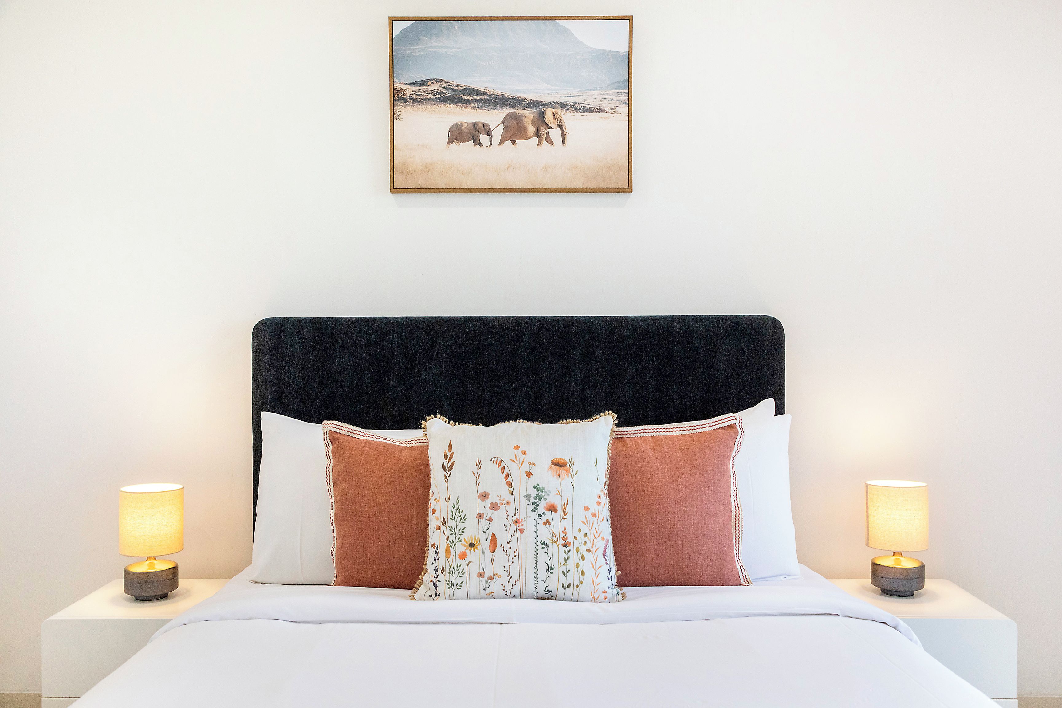 A hotel room with a bed, two bedside lamps, a framed picture on the wall, and a headboard.