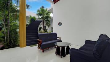 A modern outdoor seating area with a sofa and a small table, surrounded by plants and a staircase.