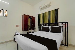 Ein Hotelzimmer mit einem Bett, einem Schrank, einem Schreibtisch mit Stuhl und einem fenster mit Vorhängen.