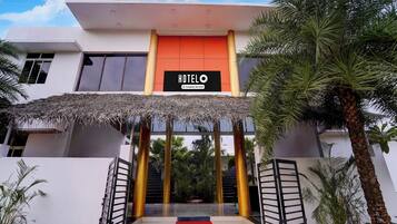 A hotel entrance with a sign, a red carpet, and a thatched roof.