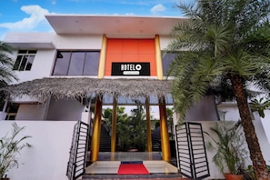 A hotel entrance with a sign, a red carpet, and a thatched roof.