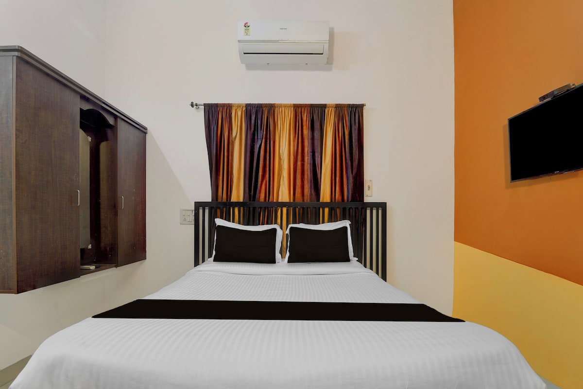 A hotel room with a bed, a wardrobe, an air conditioning unit, and a television mounted on the wall.