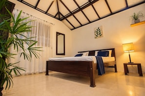A bedroom with a bed, a bedside table with a lamp, a mirror, and a potted plant.