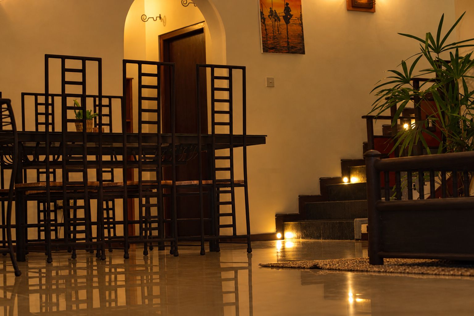 A room with a dining table and chairs, a staircase, and a potted plant.