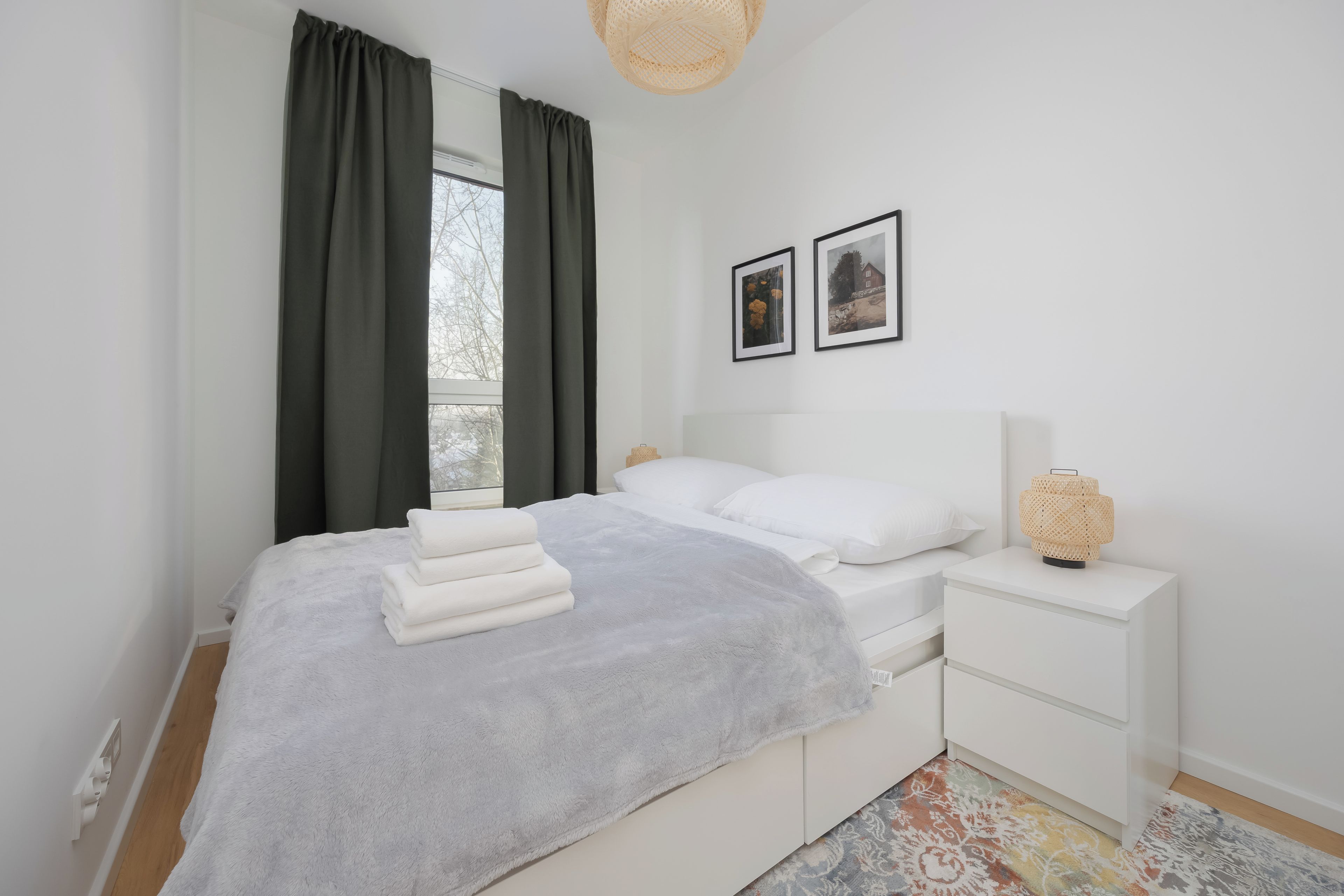 Un dormitorio moderno con cama, mesitas de noche blancas, una manta gris y dos cuadros en la pared.