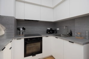 A compact kitchen with white cabinets, a built-in oven, a coffee maker, and a sink.