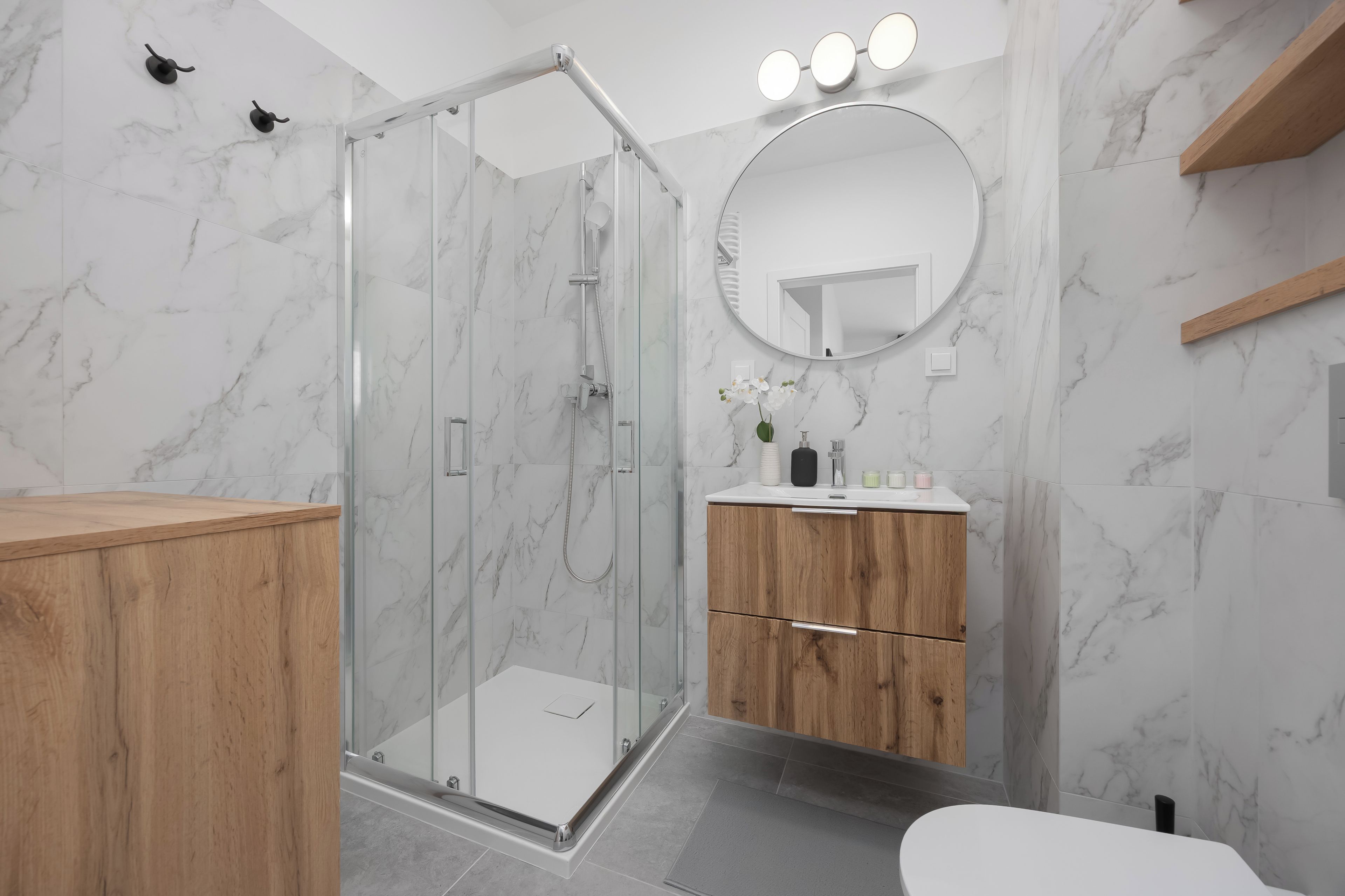 A modern bathroom with a glass-enclosed shower, a wooden vanity, and a round mirror.