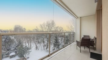 Un balcón con vistas a un paisaje nevado, barandilla de cristal y zona de estar con sillas.