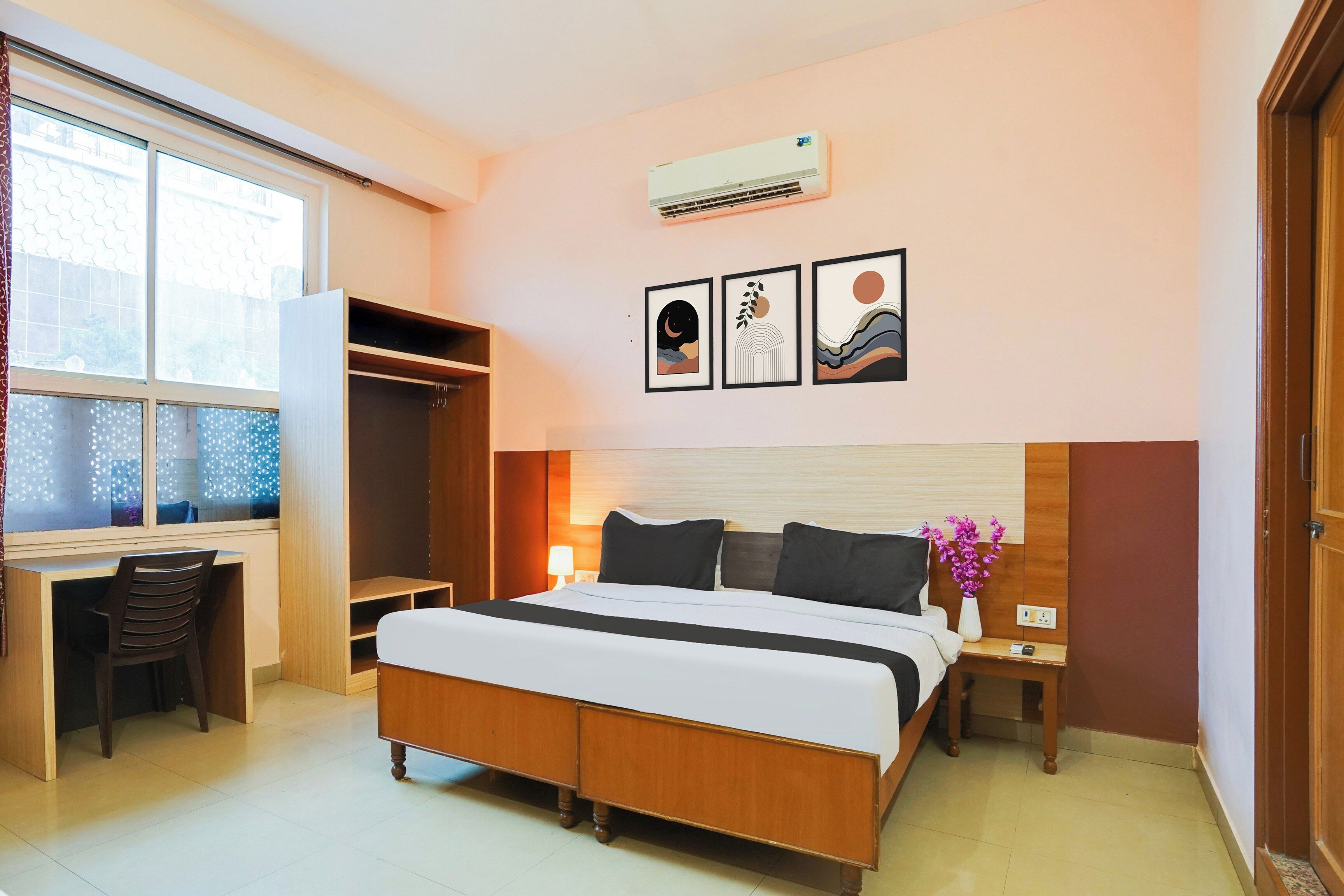 Habitación de hotel con cama, escritorio y armario. Tres obras de arte enmarcadas decoran la pared.