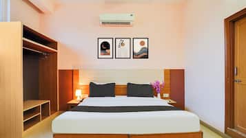 A hotel room with a bed, a wardrobe, a nightstand, a lamp, and three framed artworks on the wall.