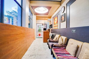 Eine Hotelhalle mit einer Rezeption, einer Wartezone mit Polstersitzgelegenheiten und Blick durch das Fenster.