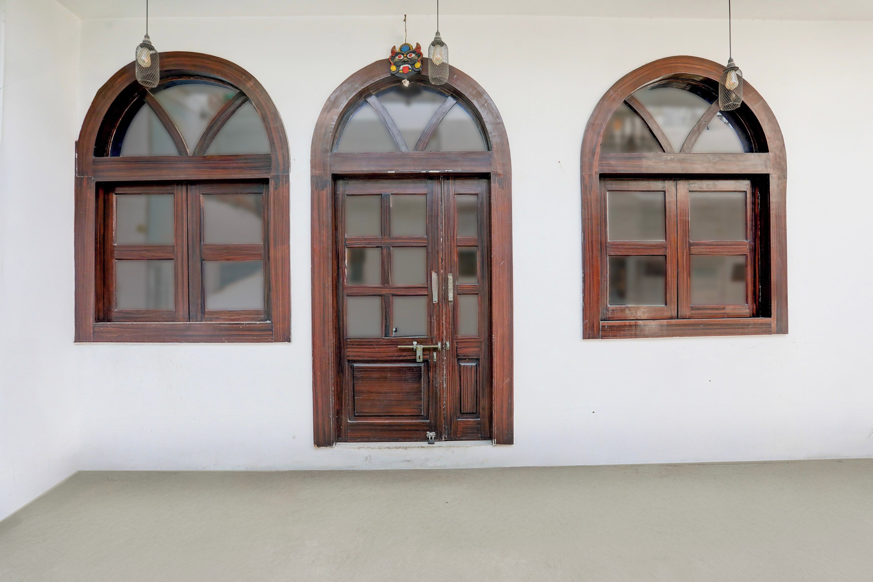 Three arched windows with wooden frames and glass panes, mounted on a plain wall.