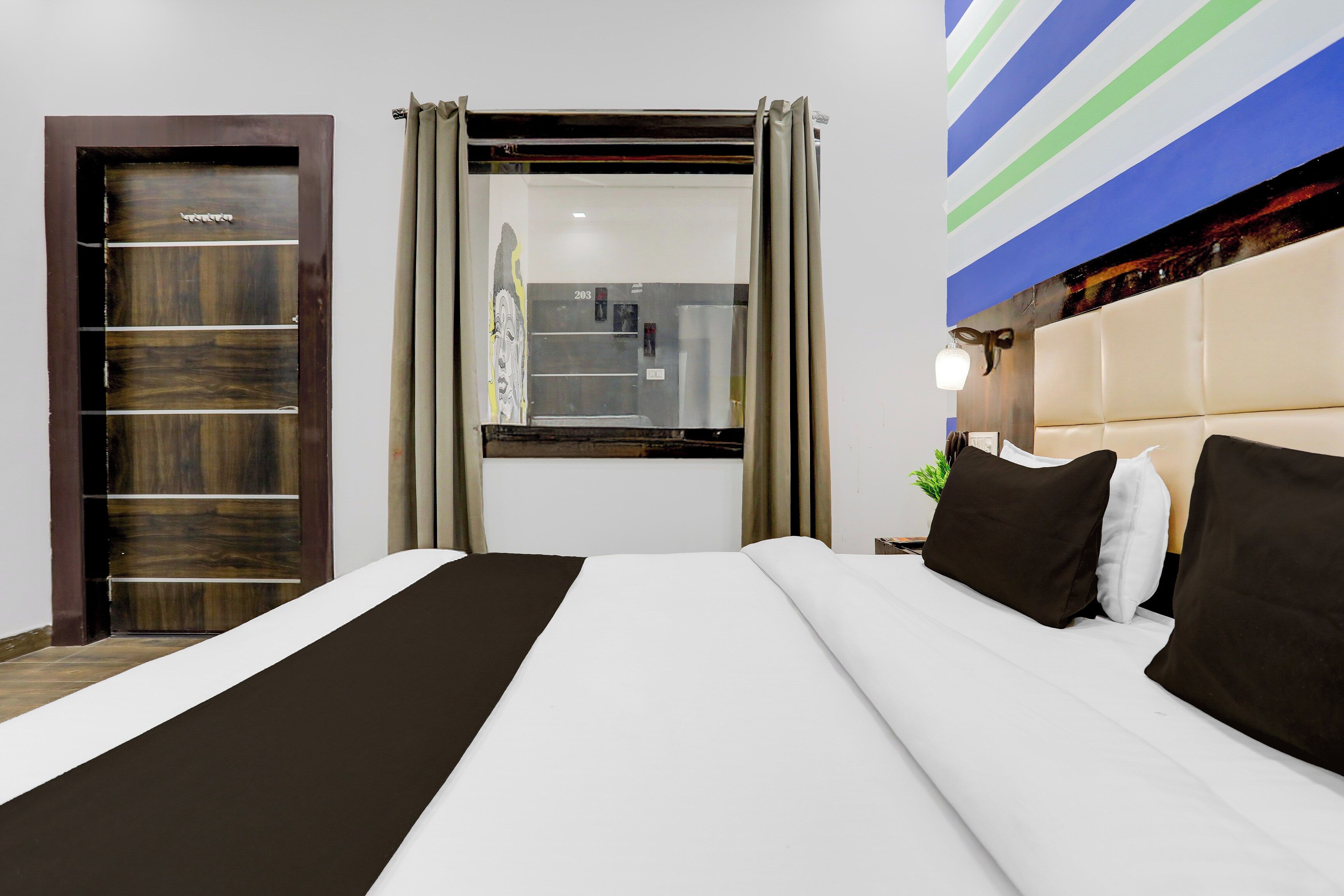 A hotel room with a bed, a wardrobe, a window with curtains, and a wall with a striped design.