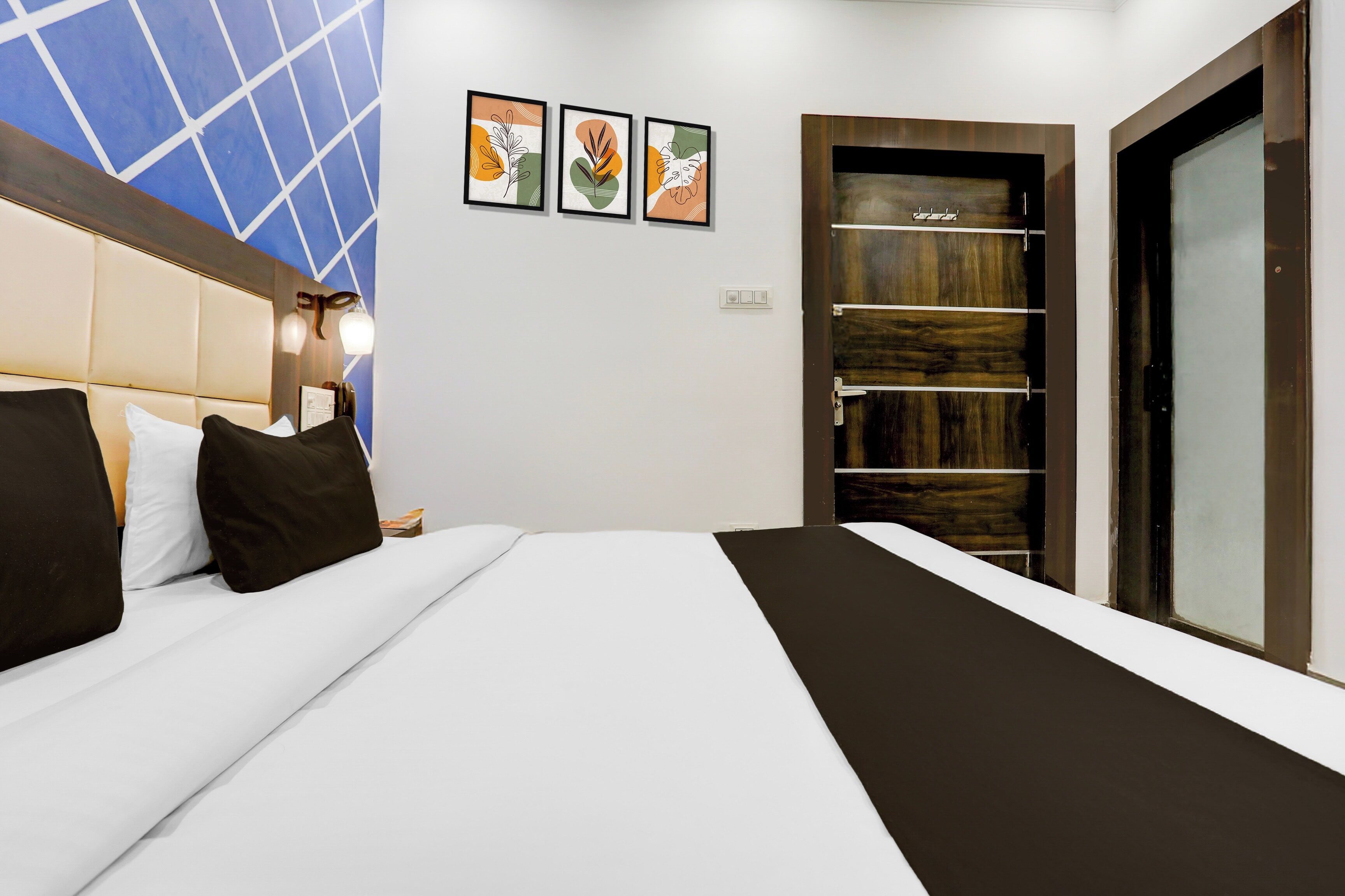A hotel room with a bed, a nightstand, a wall-mounted lamp, and a door with a wooden panel.