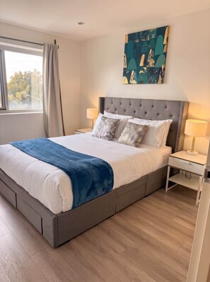 Quarto moderno com uma cama grande, duas mesas de cabeceira, encosto e janela com cortinas.