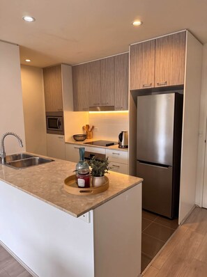 A modern kitchen with a stainless steel refrigerator, double sink, and wooden cabinets. - Braddon Luxe Retreat ,Parking, Gym & City Views (Braddon)