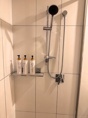 A shower with a handheld showerhead and a wall-mounted faucet, a control panel, and three bottles of shampoo and conditioner on a shelf. - Braddon Luxe Retreat ,Parking, Gym & City Views (Braddon)
