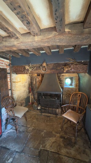 A rustic interior with exposed wooden beams, a stone fireplace, and two wooden chairs. - Farmhouse Sleeps 13 With Hot Tub (Crewkerne)