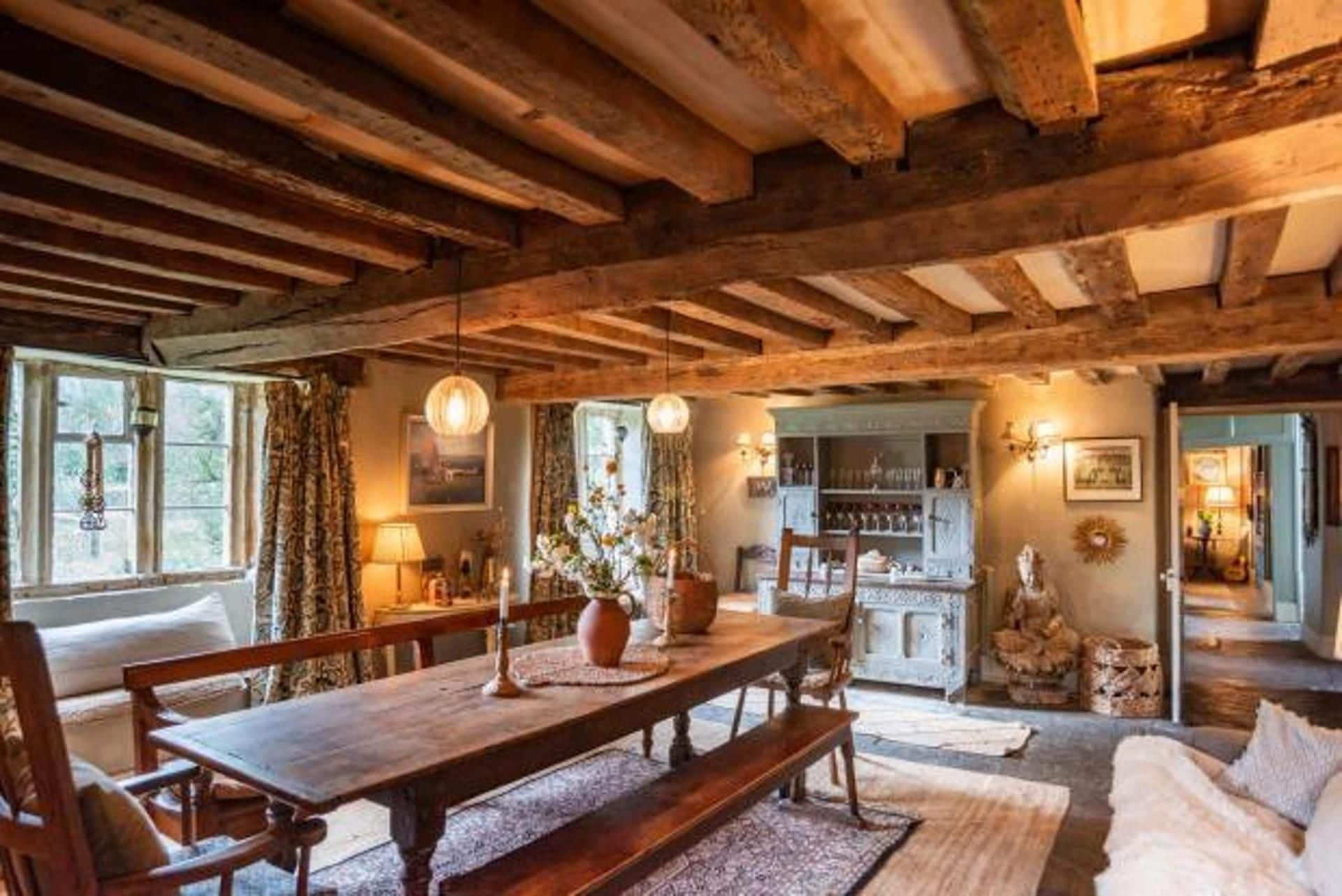 Un intérieur rustique avec des poutres apparentes, une table à manger en bois, des bancs et un coin salon confortable.