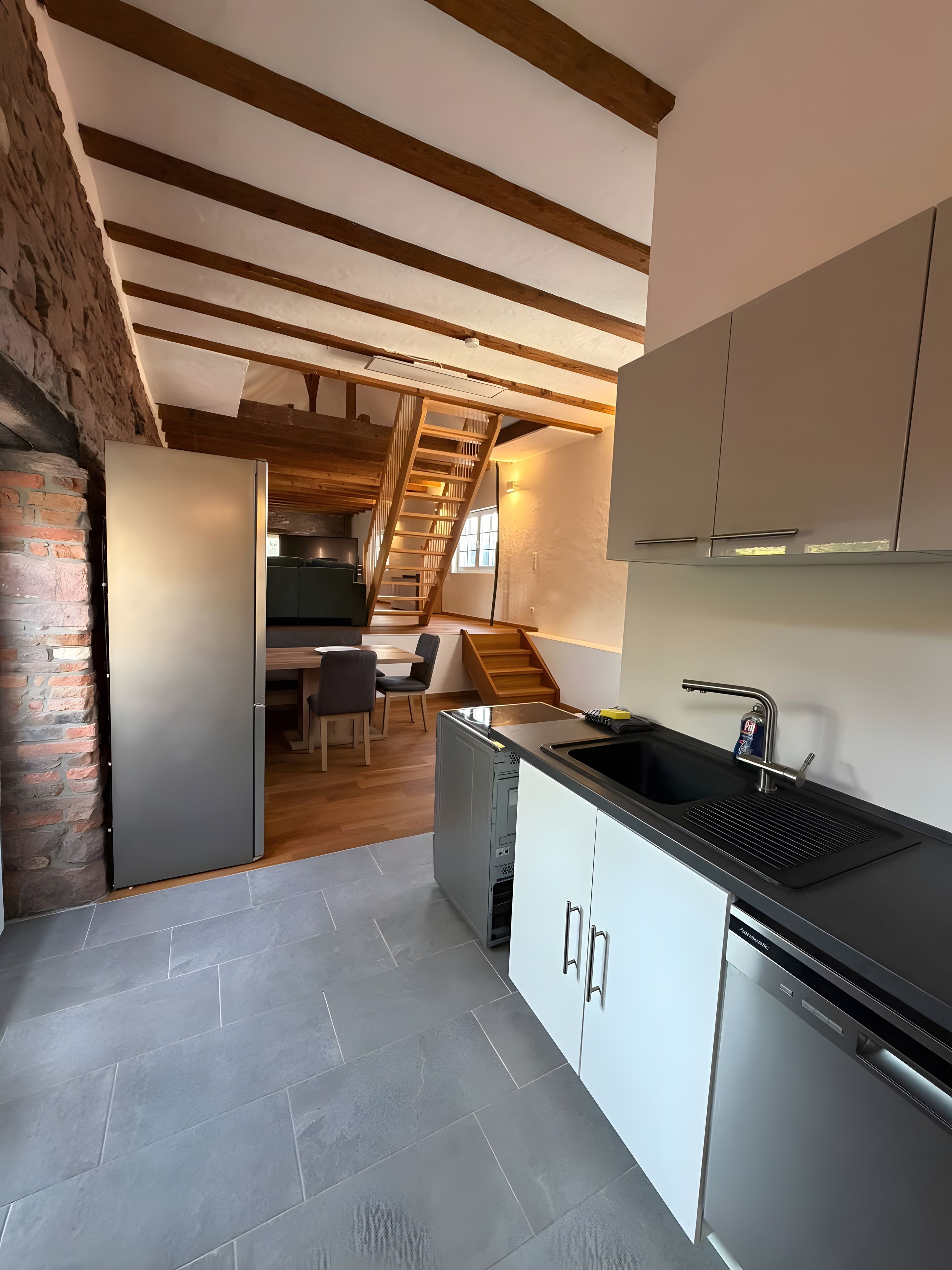 Una cocina moderna con lavavajillas integrado, una escalera de madera y un comedor con mesa y sillas.