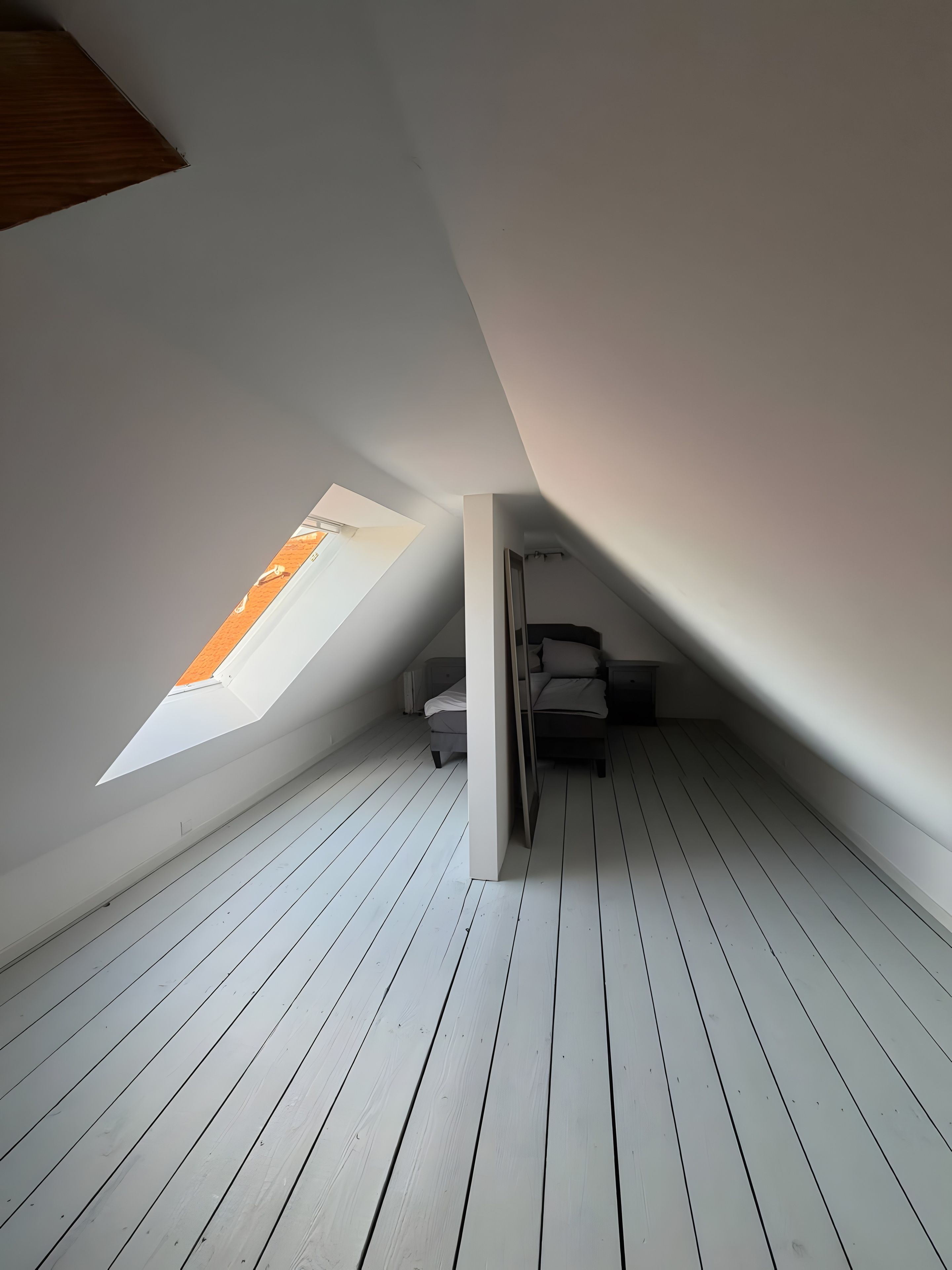 Ein Zimmer mit schrägem Dach und einem Oberlicht sowie einem Bett.