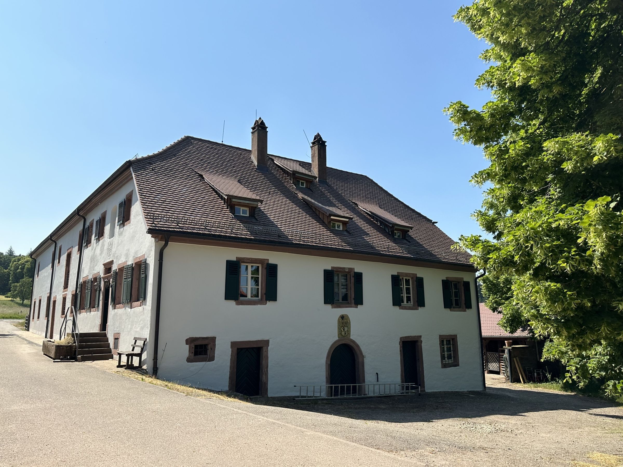 A two-story building with a pitched roof, multiple windows with shutters, and a central entrance with an archway.