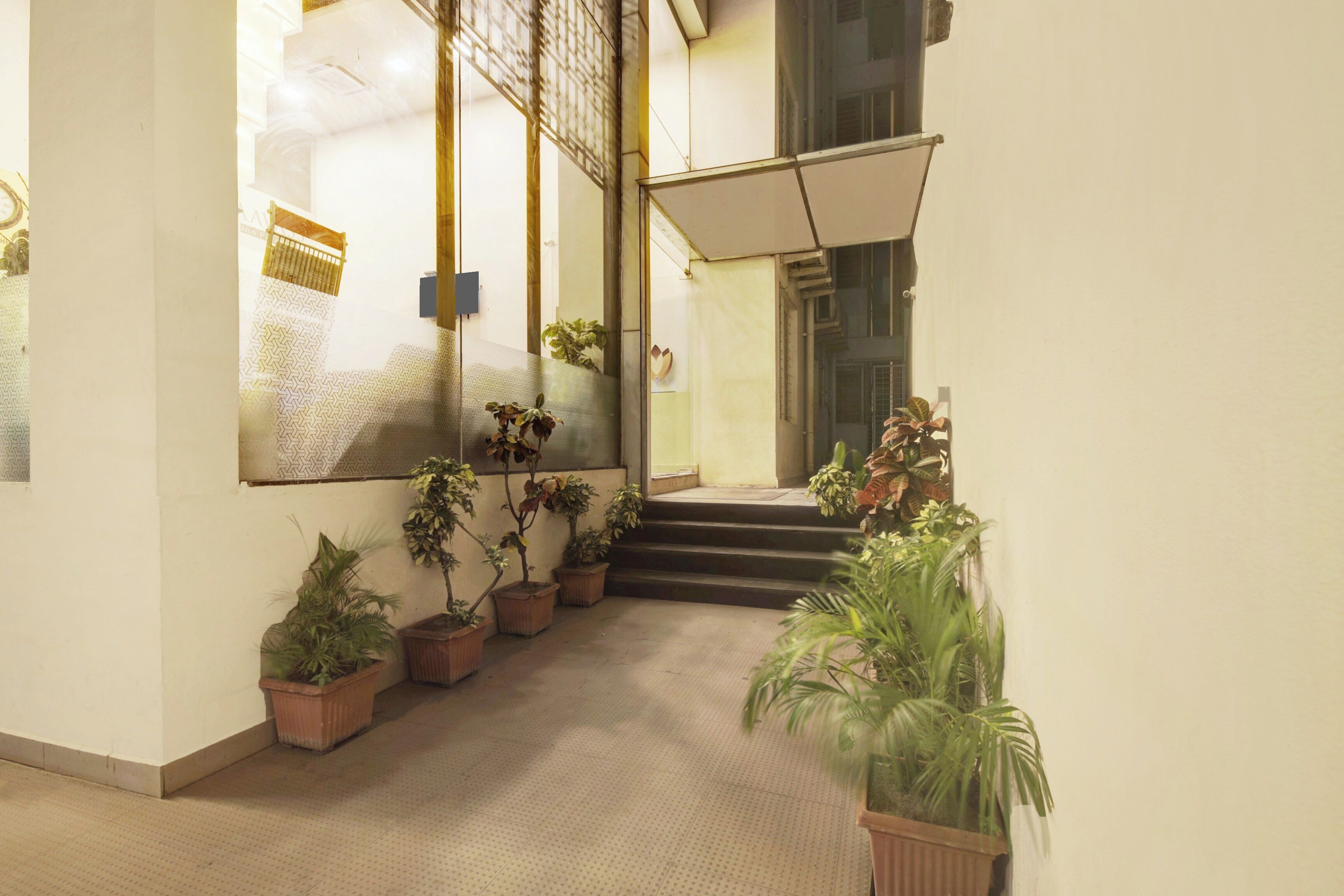 Un pasillo con plantas en macetas, una escalera y una puerta de cristal que da a otra habitación.