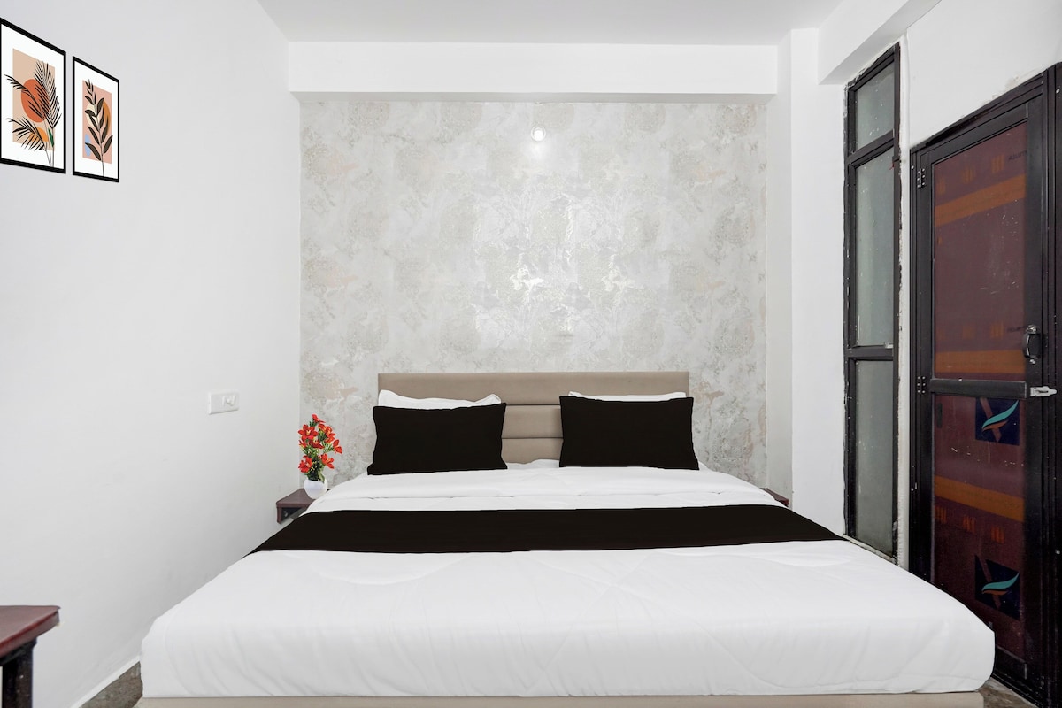 Un dormitorio con cama, mesita de noche, un jarrón con flores y una puerta.