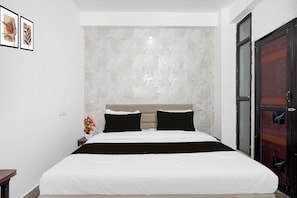 Un dormitorio con cama, mesita de noche, un jarrón con flores y una puerta.