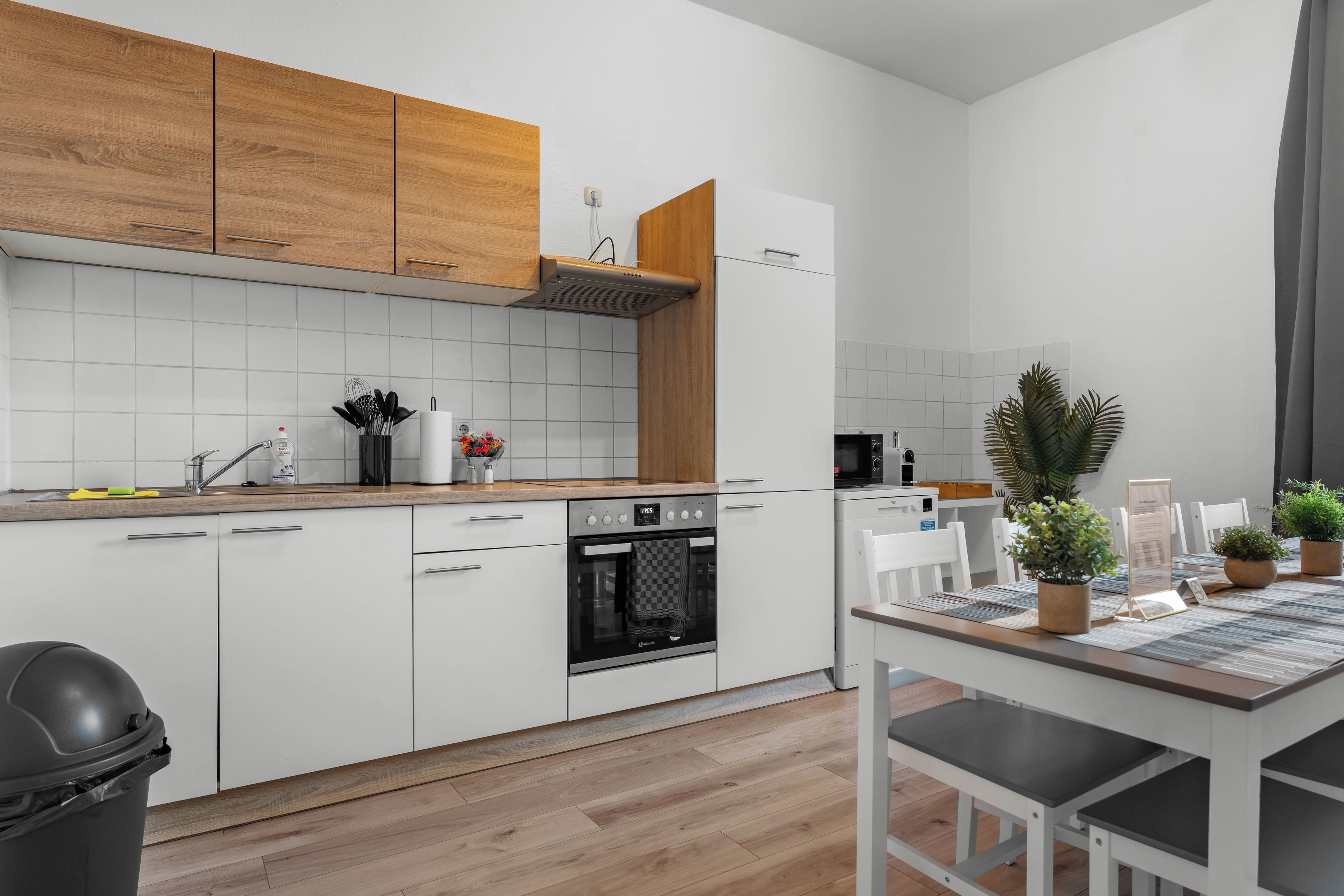 A modern kitchen with white cabinetry, a wooden countertop, a built-in oven, and a dining area with a table and chairs.