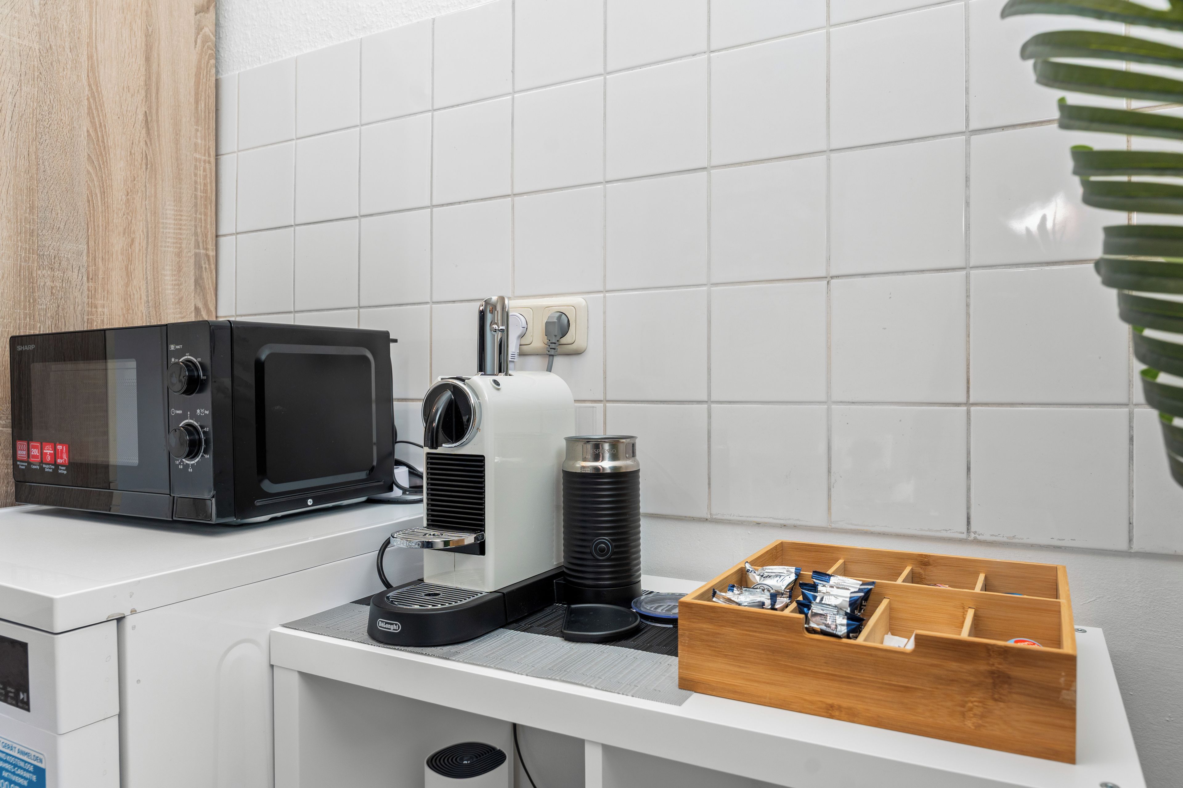 A kitchen area with a microwave, coffee machine, and a drawer with coffee pods.