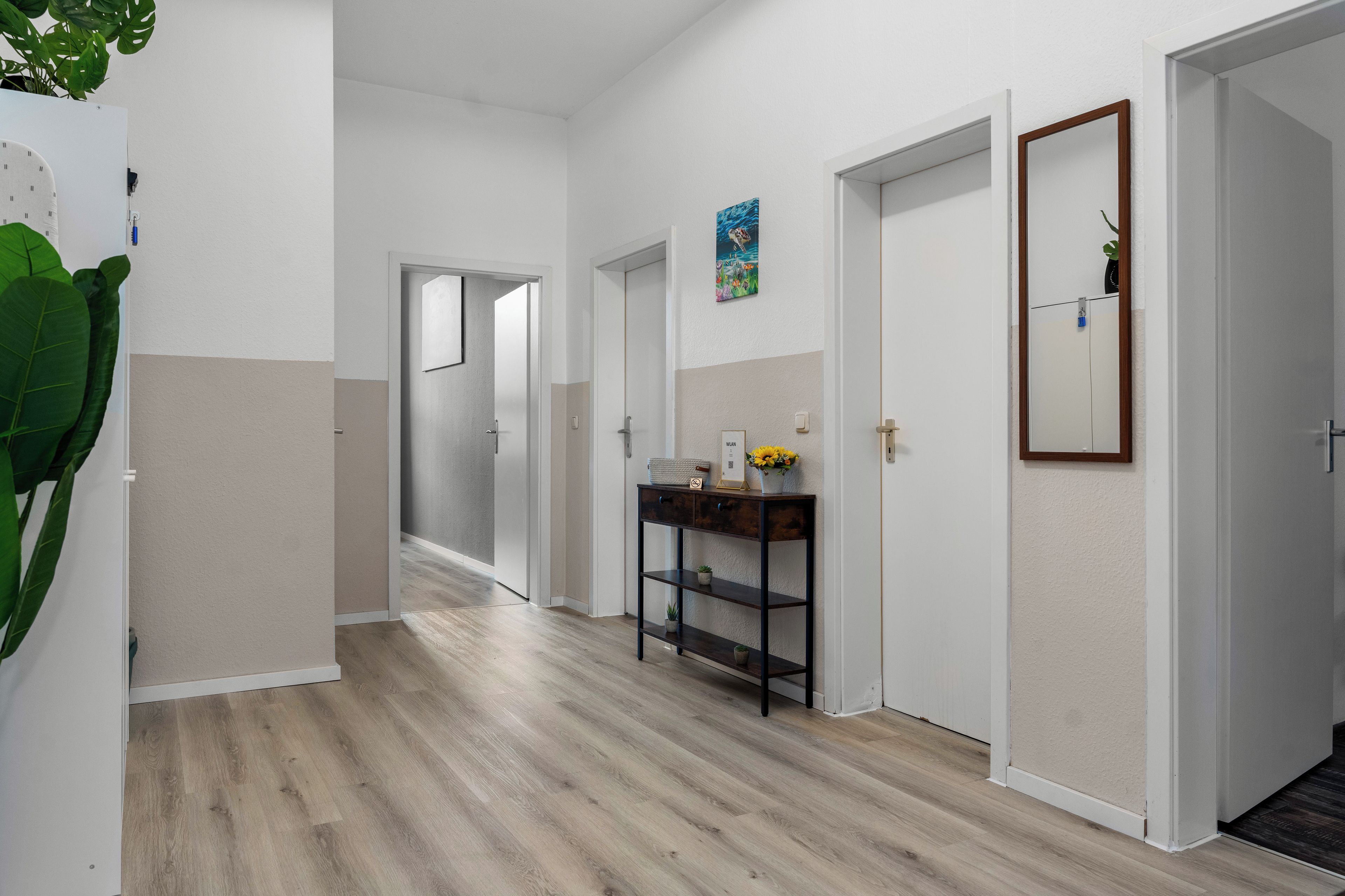 Un pasillo con suelo de madera, paredes blancas y una puerta que da a otra habitación.