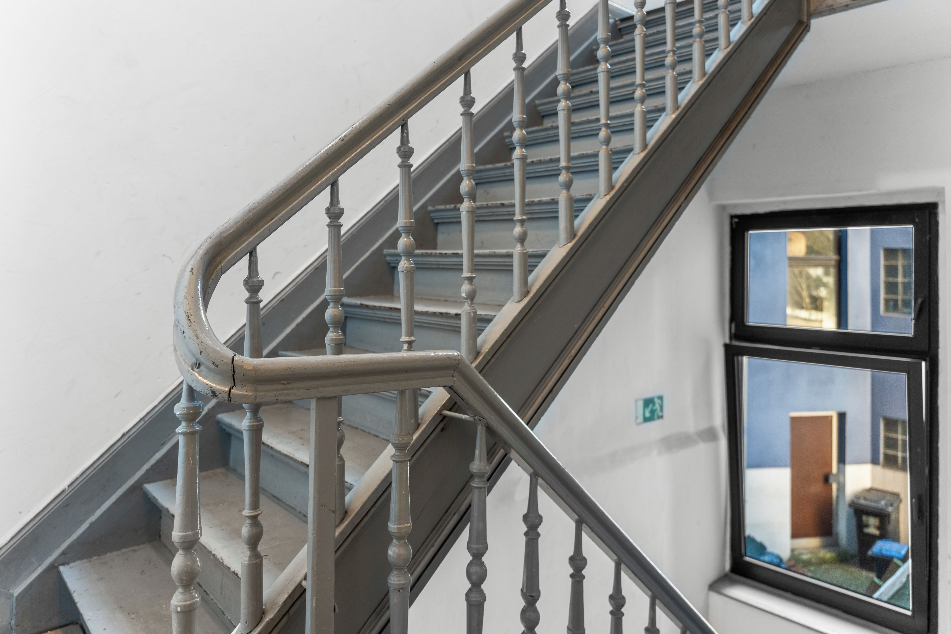 A staircase with a handrail and balusters, leading to a landing with a window.