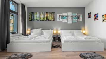 A hotel room with two beds, a large window with curtains, a wall with multiple artworks, and a wooden floor.