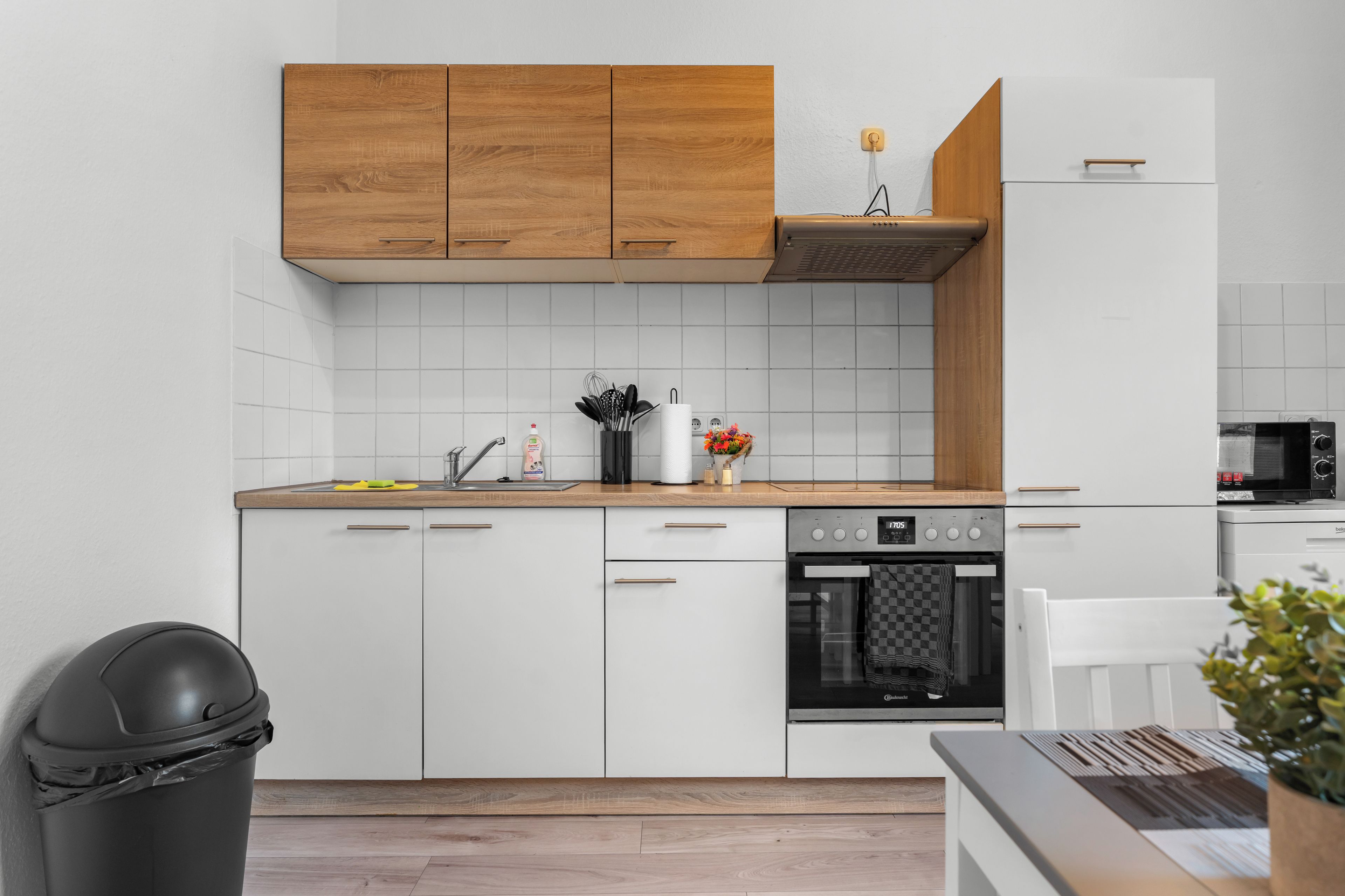 A modern kitchen with white cabinetry, a wooden upper shelf, and a built-in oven.