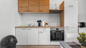 A modern kitchen with white cabinetry, a wooden upper shelf, and a built-in oven.